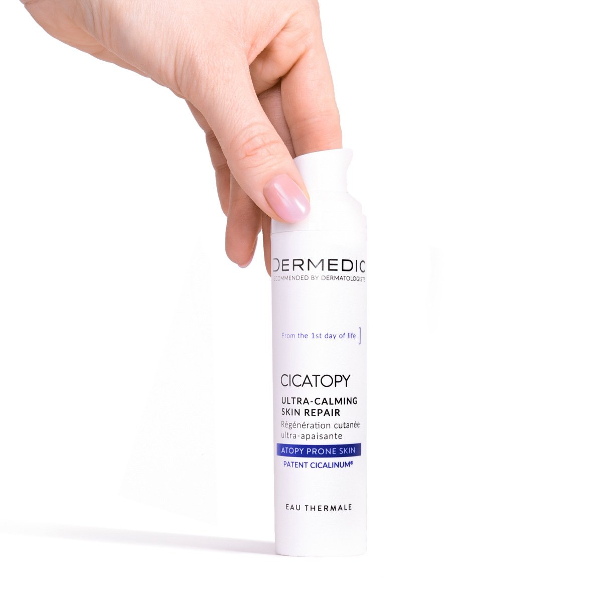 A hand holding a white bottle of Dermedic Cicatopy Ultra-Calming Skin Repair lotion against a white background. The bottle is labeled for atopy-prone skin and features blue and purple accents.