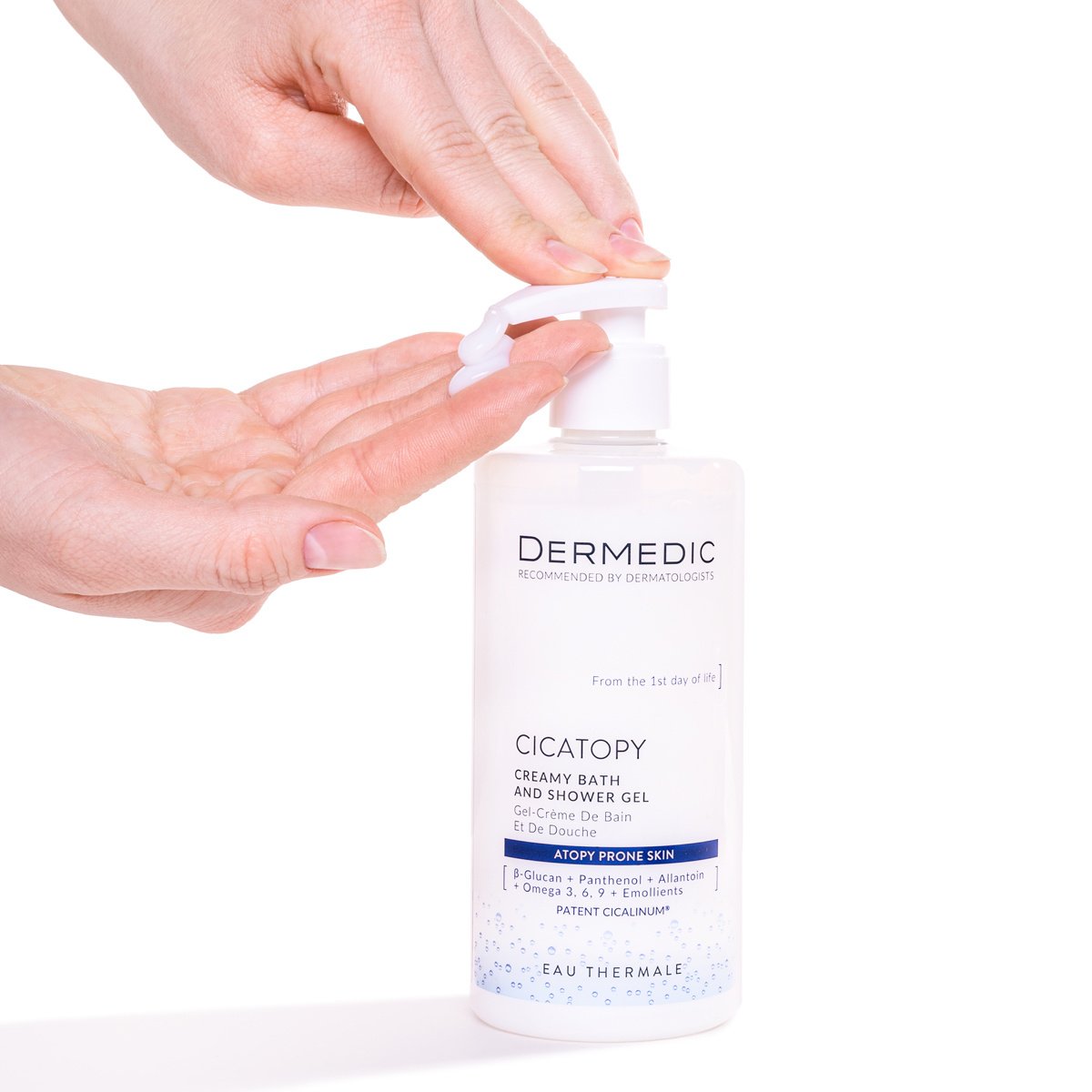 A hand presses the pump of a Dermedic CICATOPY kremowy żel do kąpieli bottle, dispensing the product onto the fingers against a white background.
