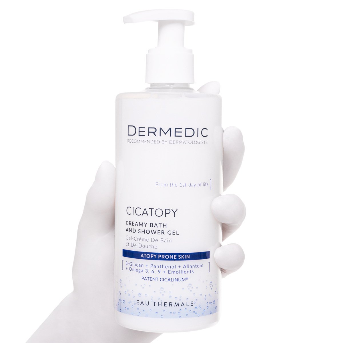 A gloved hand holds a white pump bottle of Dermedic CICATOPY kremowy żel do kąpieli, labeled for atopy-prone skin, with blue and black text on a white background.