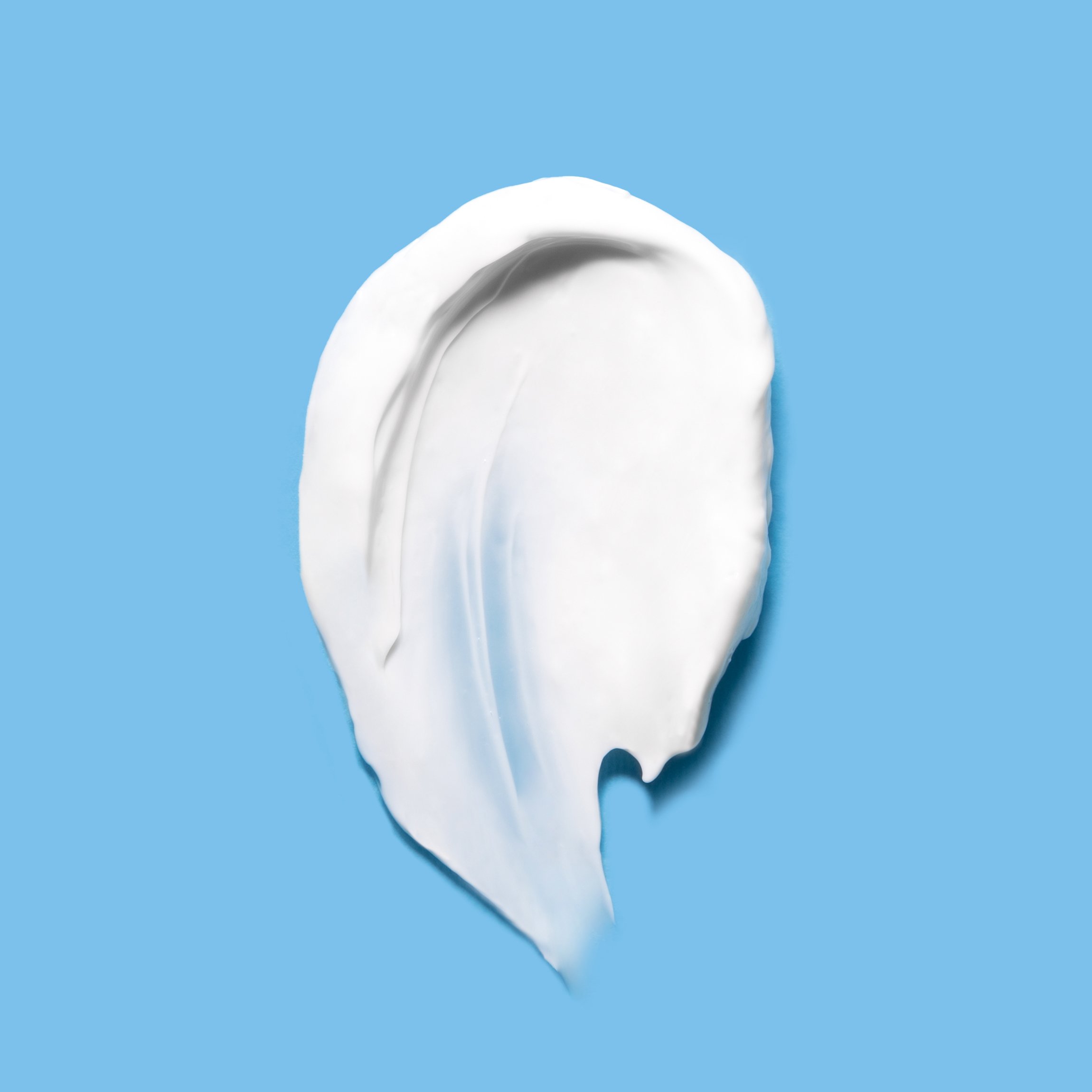 A smear of white cream or lotion is spread in an oval shape on a light blue background.