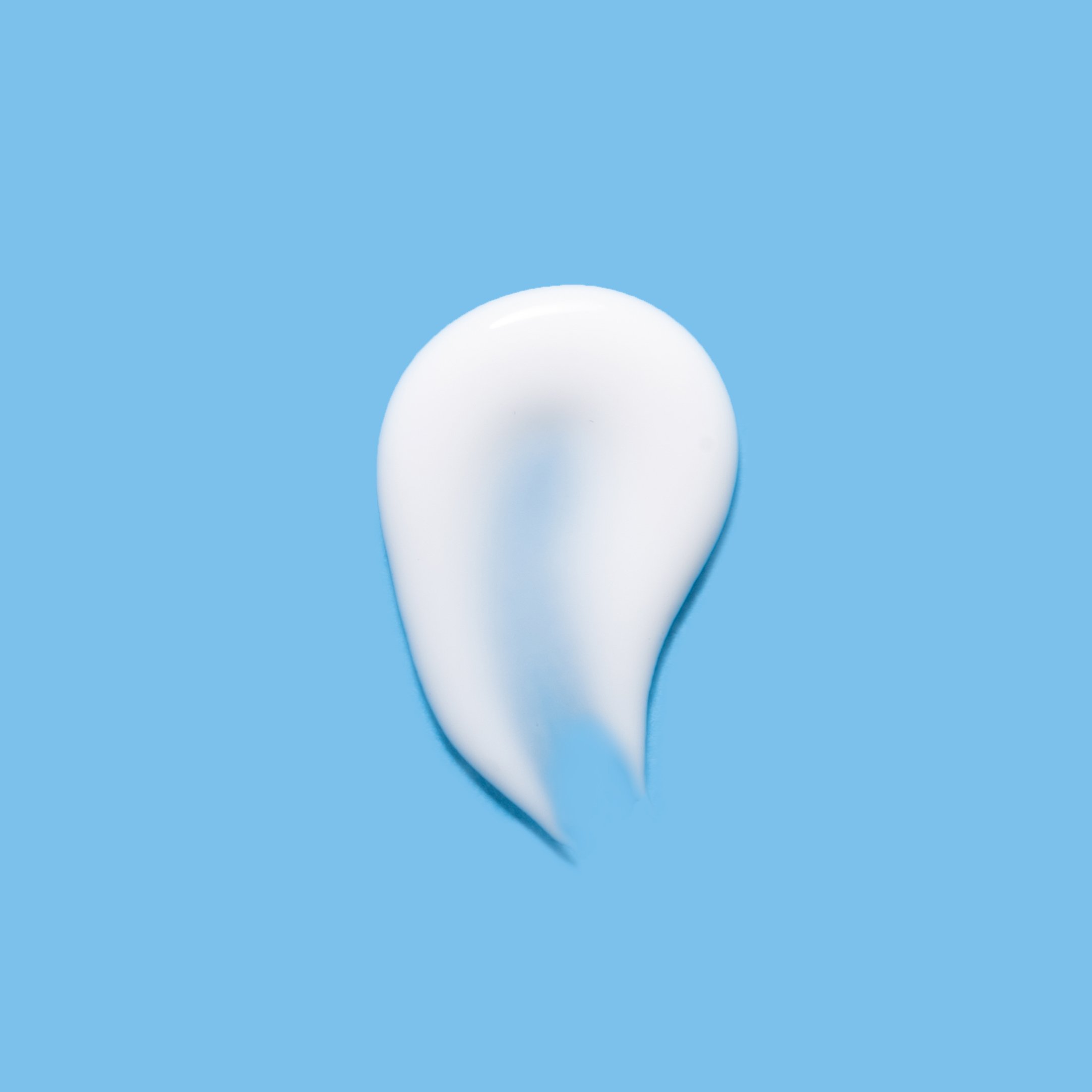 A dollop of white cream or lotion is spread in a teardrop shape on a solid light blue background.
