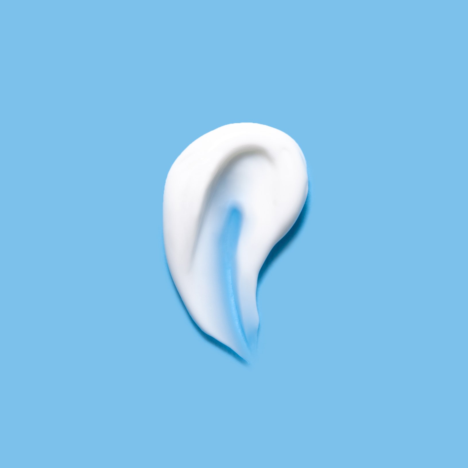 A swirl of white and blue cream is arranged in the shape of an ear on a solid light blue background.
